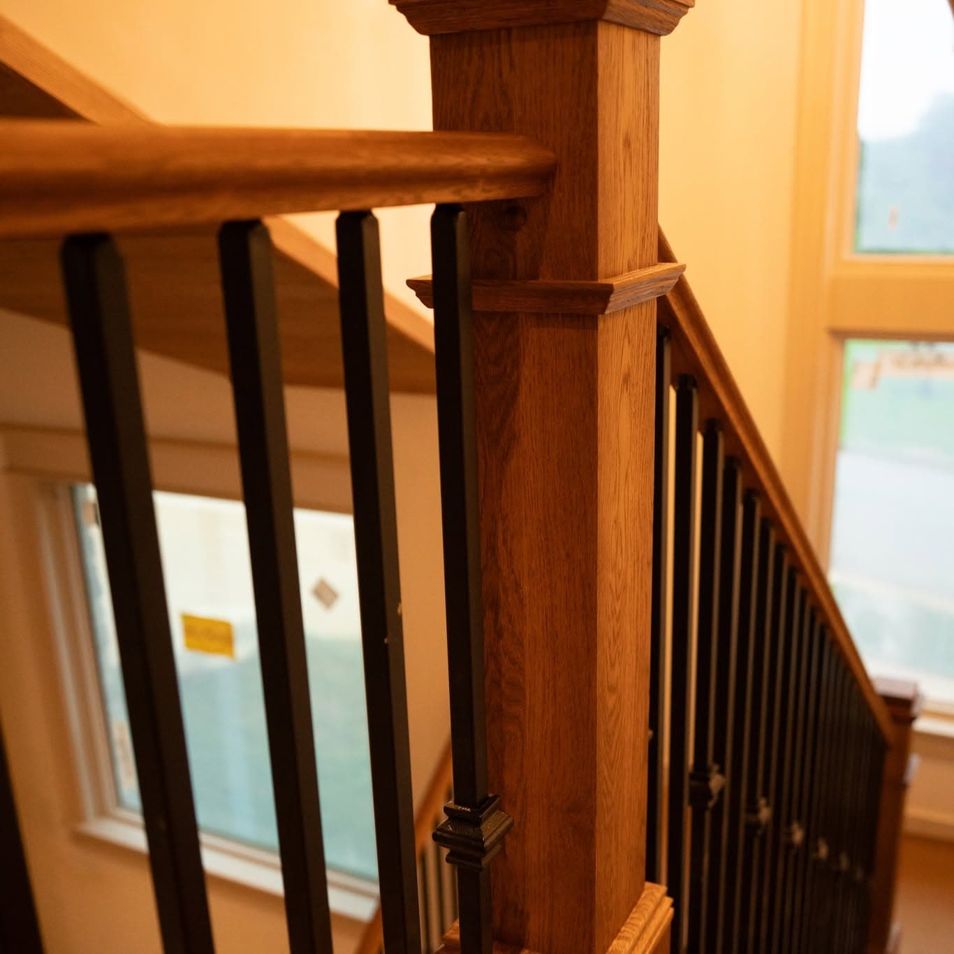 Oak newel post and handrail with black iron balusters beside tall windows, a job by Alabama Hardwood Restoration