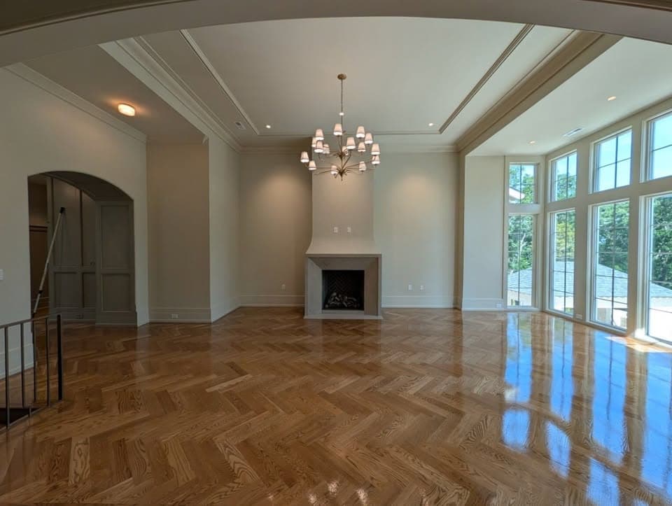High-gloss herringbone hardwood floor in a bright living room with a fireplace, a job by Alabama Hardwood Restoration