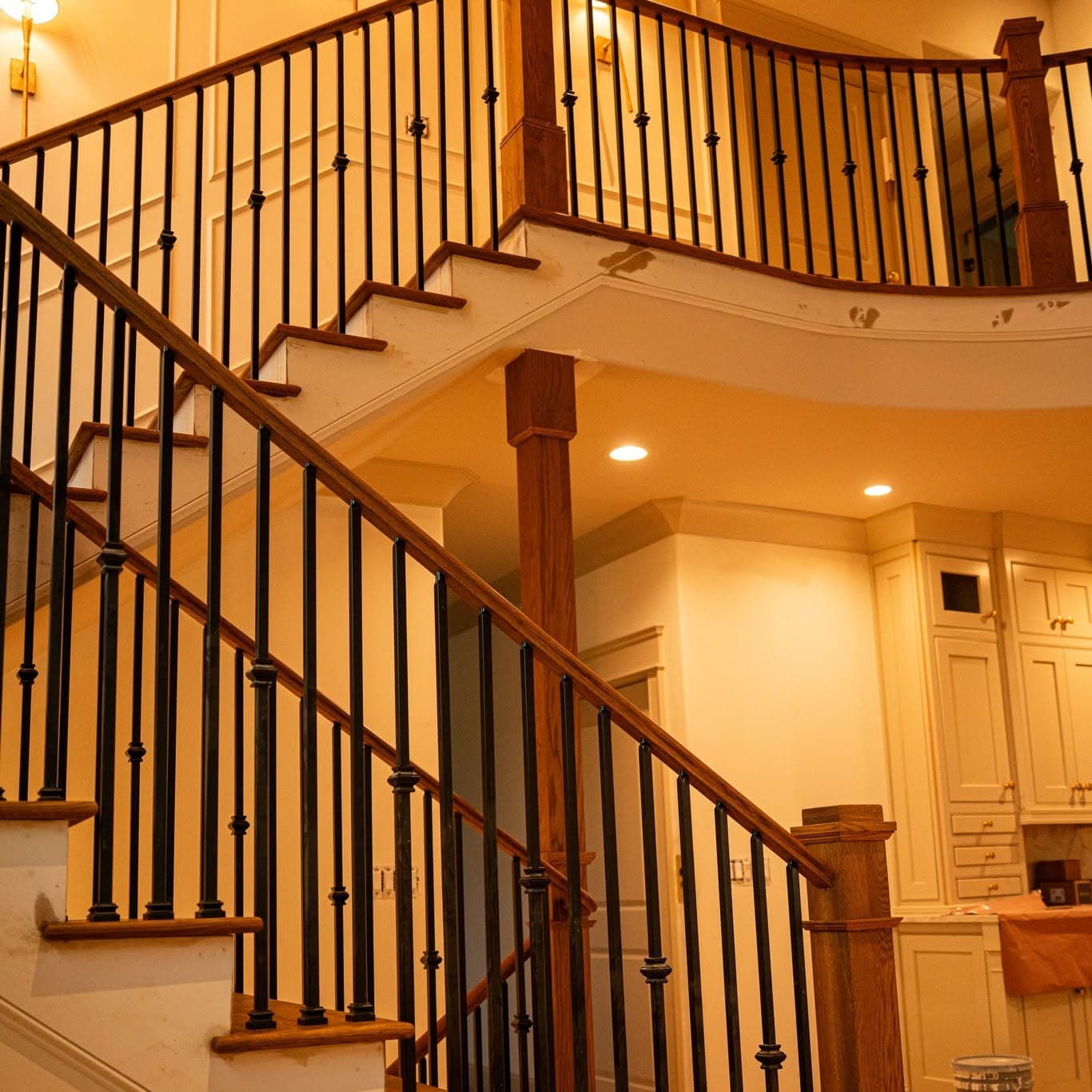 Curved hardwood staircase and upper balcony with white risers and black metal balusters, a job by Alabama Hardwood Restoration