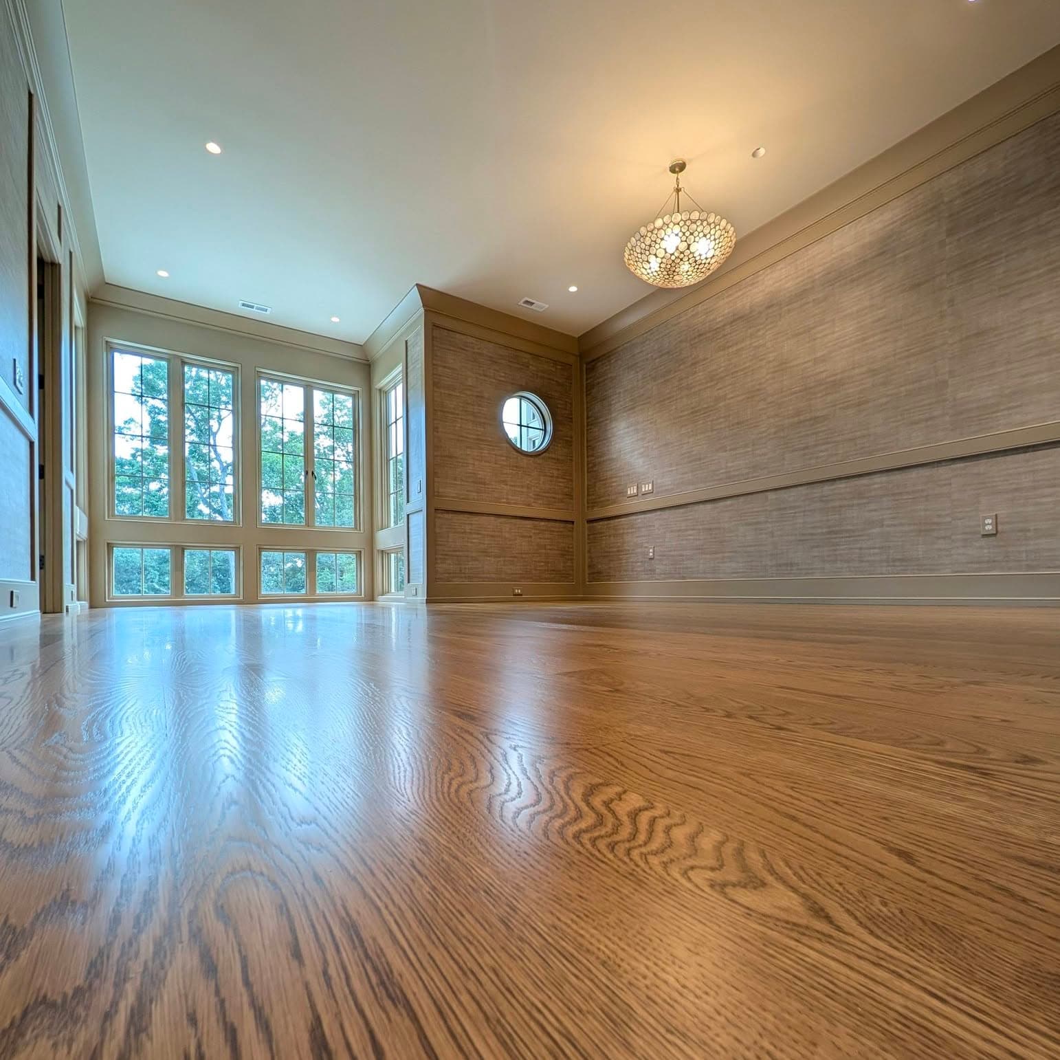 Warm stained oak hardwood floor in a room with grasscloth wallpaper and large windows, a job by Alabama Hardwood Restoration