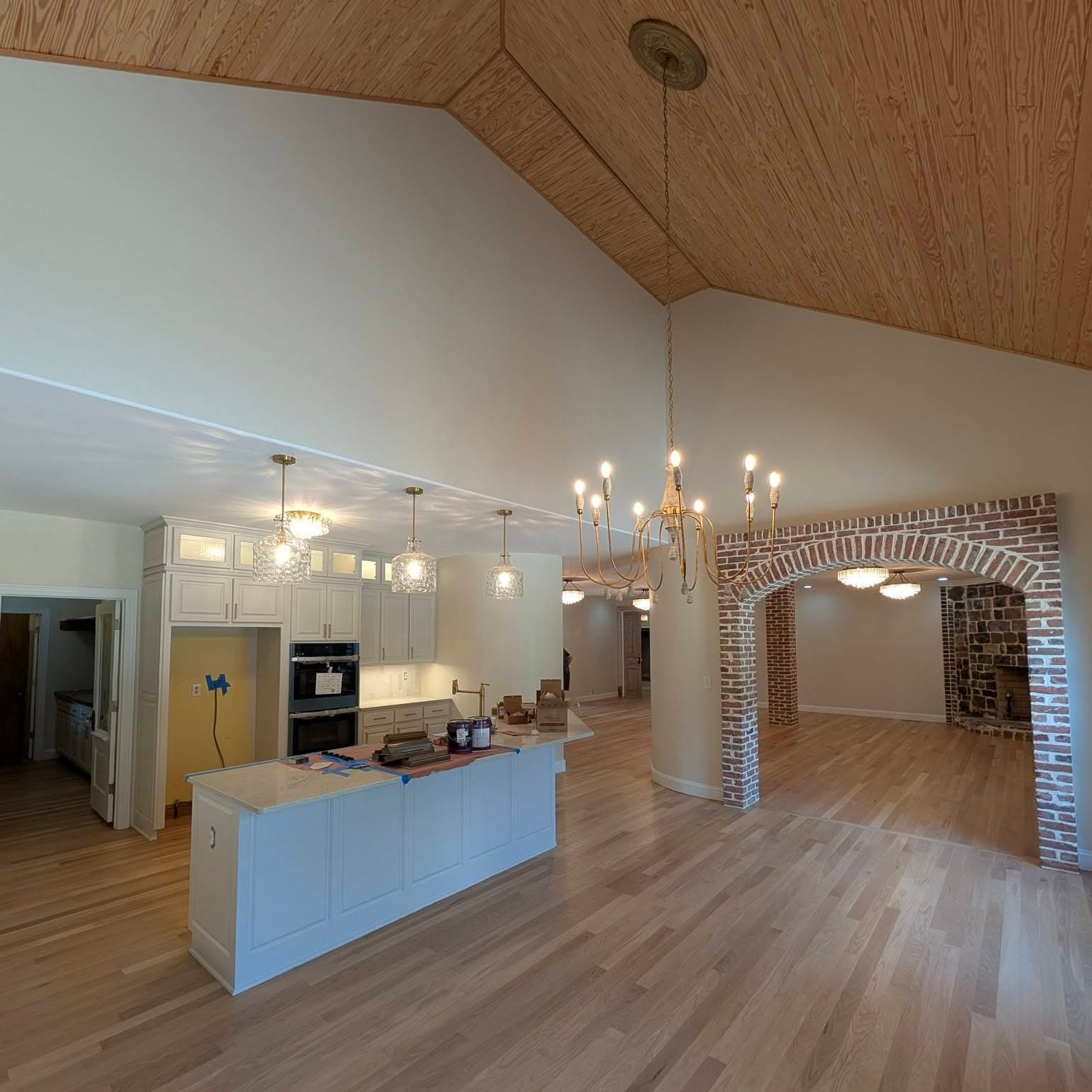 Light oak hardwood flowing from a white kitchen through a brick arch into a living room, a job by Alabama Hardwood Restoration
