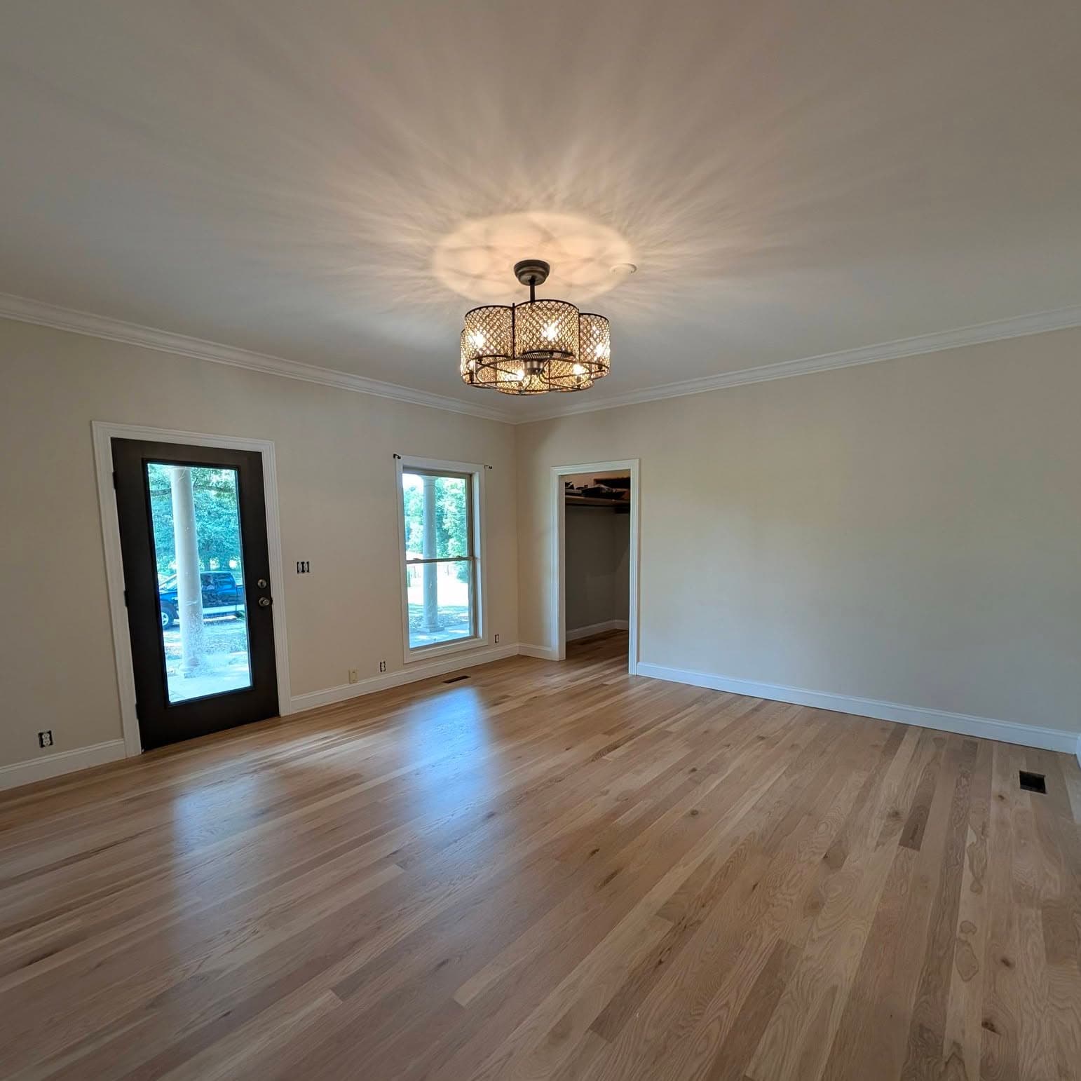 Light-toned wide-plank oak floor in an empty living room with a drum chandelier, a job by Alabama Hardwood Restoration