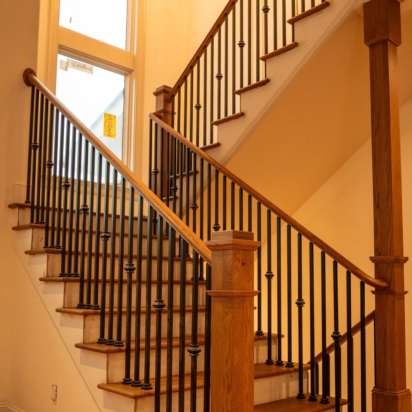 Hardwood stair treads with cream risers, matching handrail, square wood newels, and matte black metal balusters, a job by Alabama Hardwood Restoration