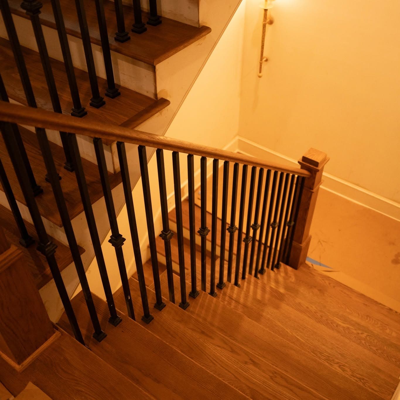 Hardwood staircase landing with matching wood newel, handrail, and matte black metal balusters, a job by Alabama Hardwood Restoration